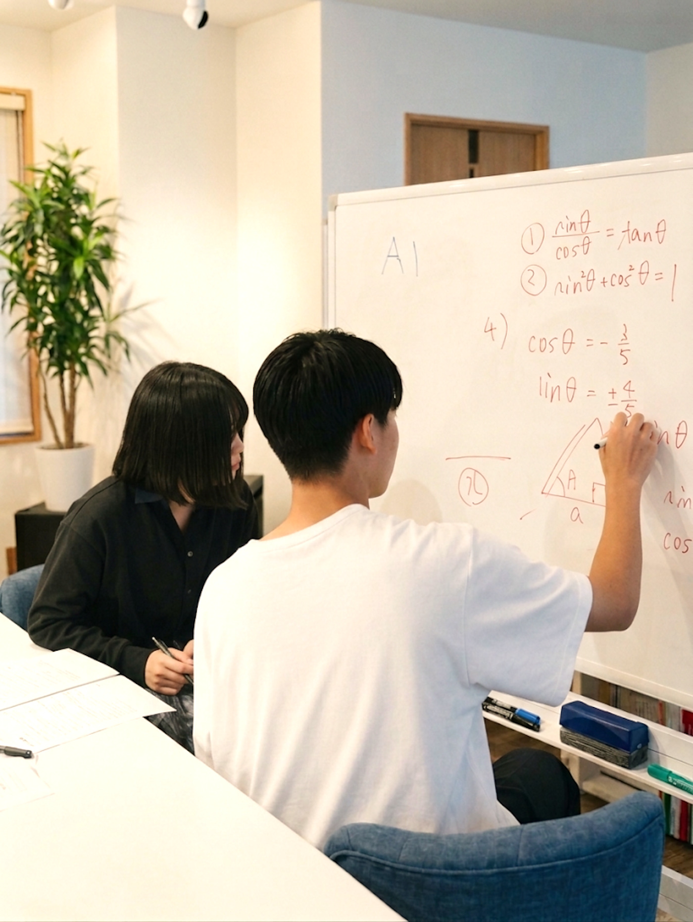ホワイトボードで三角比の解き方を説明する講師と、隣で聞く生徒